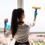 people, housework and housekeeping concept. Happy woman in gloves cleaning window with rag and cleanser spray at home